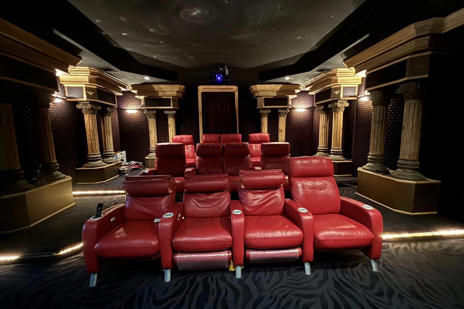 Private cinema room with tiered red leather recliners, columned walls and a painted star ceiling